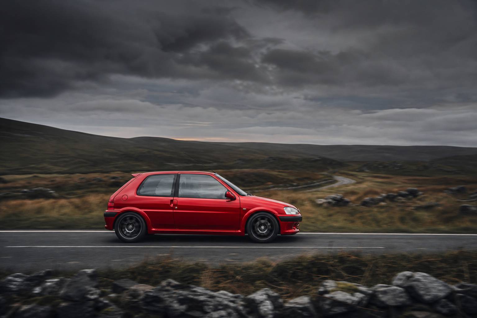 Peugeot 106 S16 rouge en vue de profil sur une route de campagne
